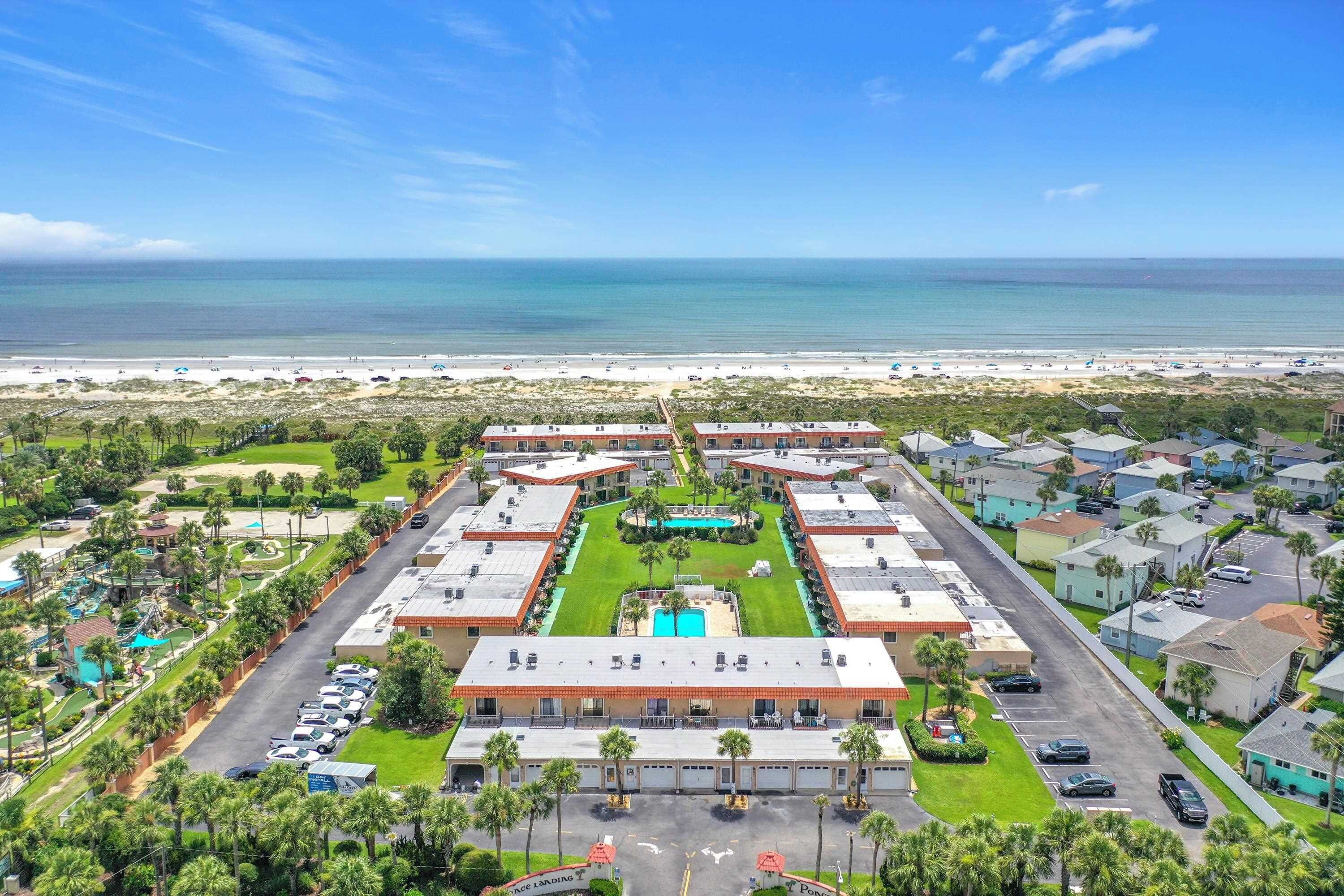 A hotel with a central pool, multiple buildings, and a beach view.