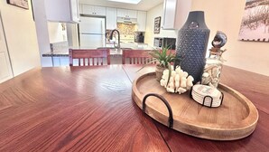 A wooden dining table with a tray holding decorative items, a kitchen in the background, and a ceiling fan. - Private Beach Access, Steps from Ocean, Heated Pool, Garage, Beach towels/chairs (St. Augustine)