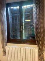 Una stanza con una finestra coperta da persiane, un termosifone sottostante e tende sui lati.