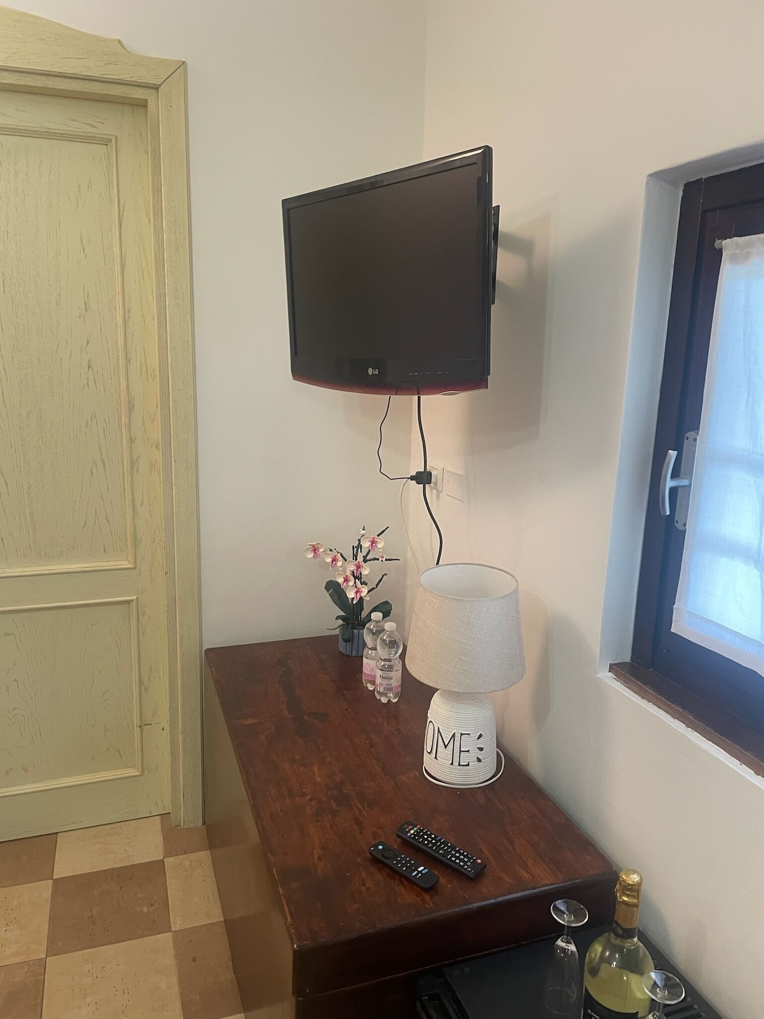 Un televisor montado en la pared, una lámpara sobre una mesa de madera y una botella de vino en el suelo.