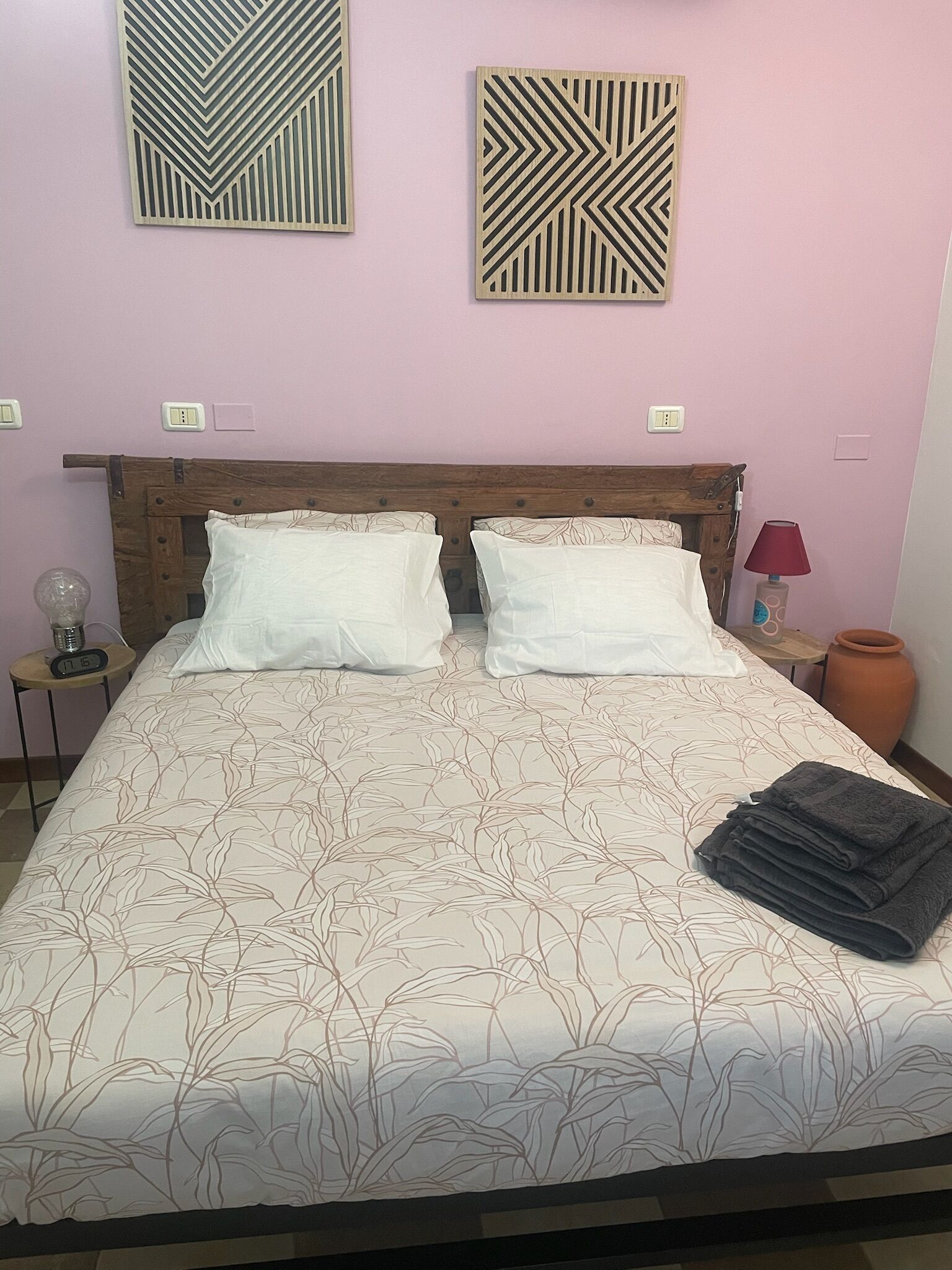 A bedroom with a bed, two wall-mounted light fixtures, a bedside table with a lamp, and a nightstand with a clock.