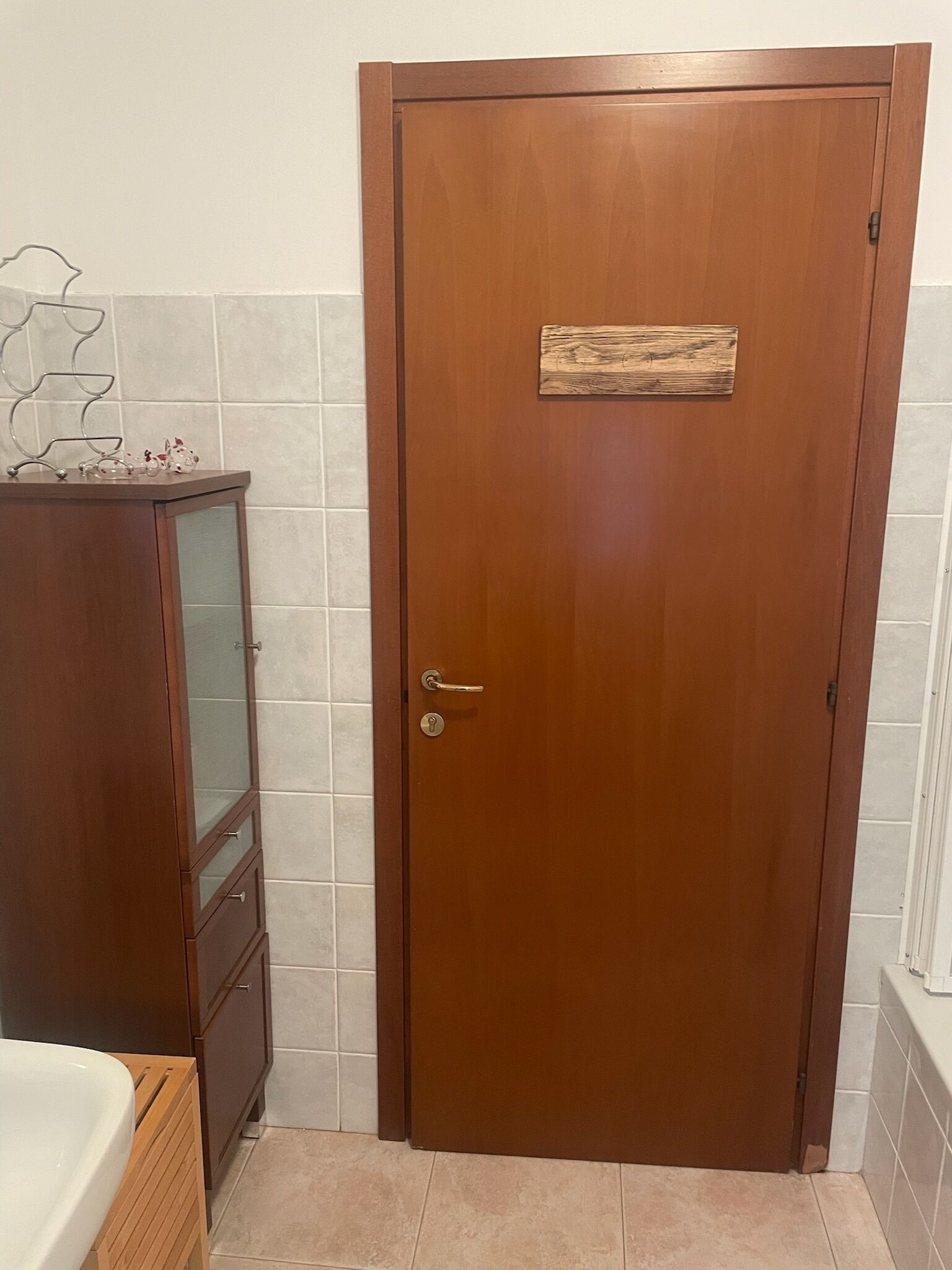 Una puerta de madera con una pequeña placa de madera, un mueble con puertas de vidrio y una pared de azulejos.