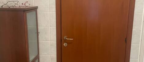Una puerta de madera con una pequeña placa de madera, un mueble con puertas de vidrio y una pared de azulejos.