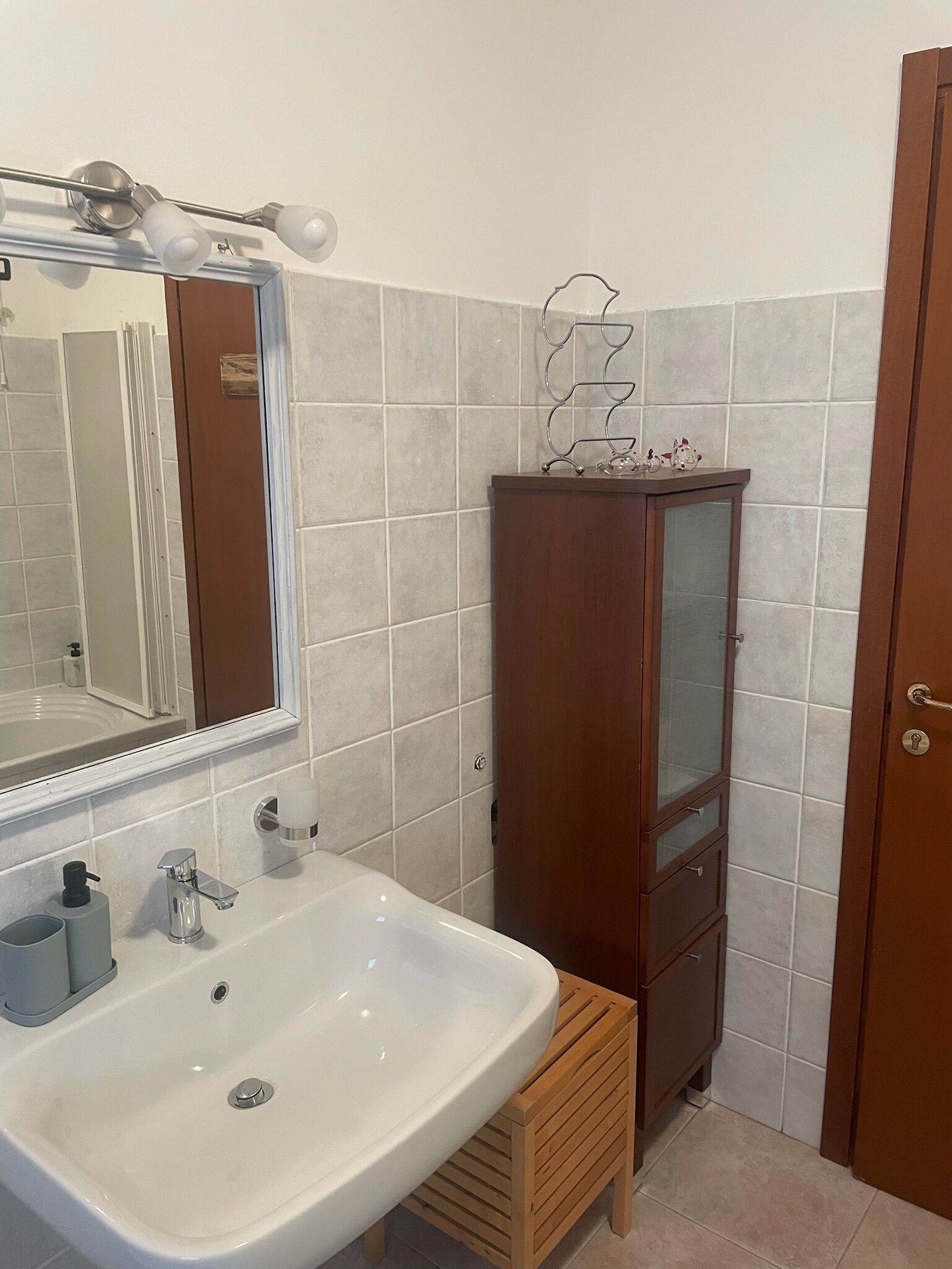 Un baño con un lavabo blanco, un mueble de madera y un espejo.