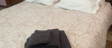 A neatly made bed with a floral-patterned bedspread, two white pillows, and a folded dark towel on the bed.