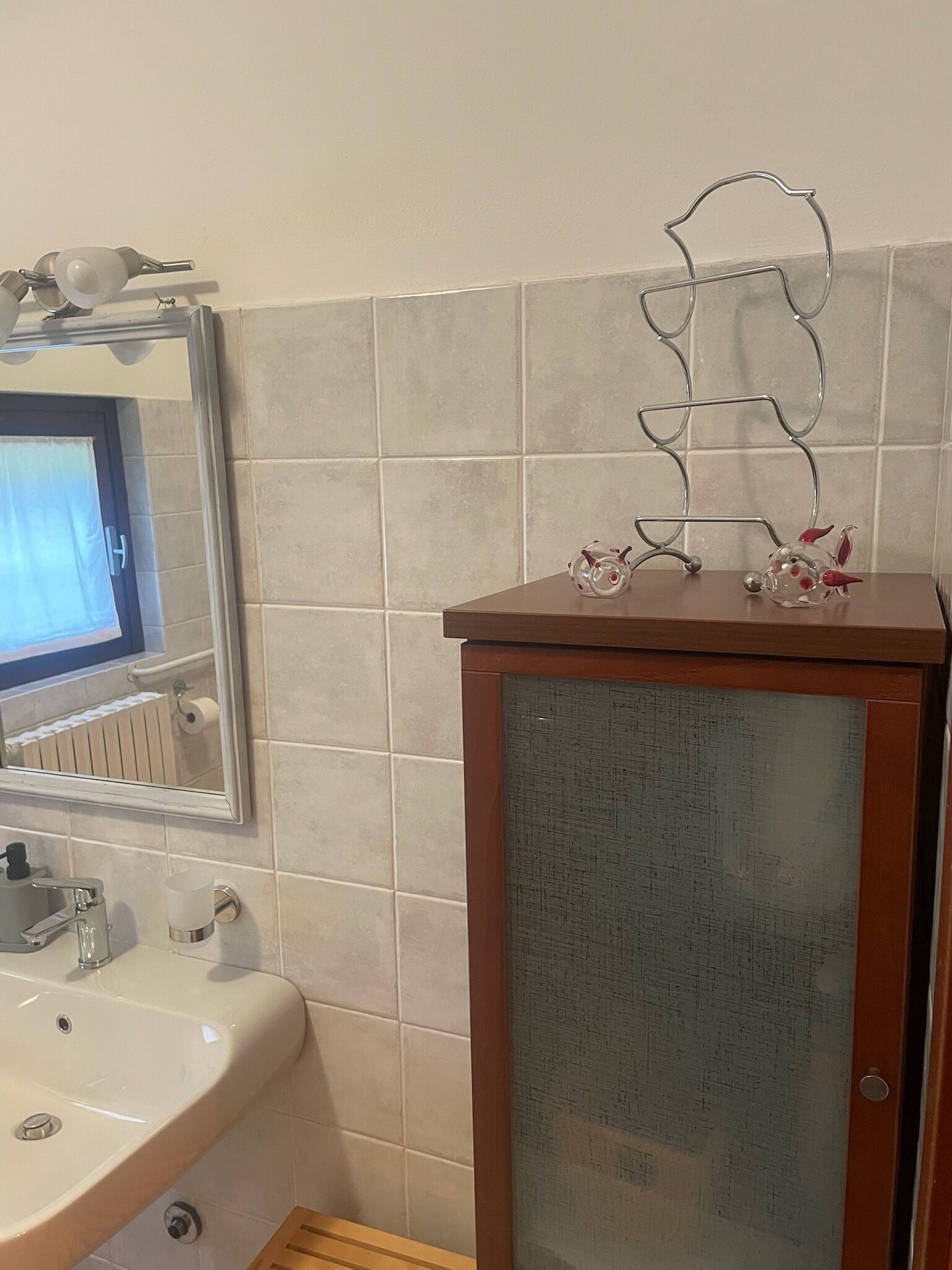 Un bagno con lavandino, specchio e un espositore metallico decorativo con statuine.