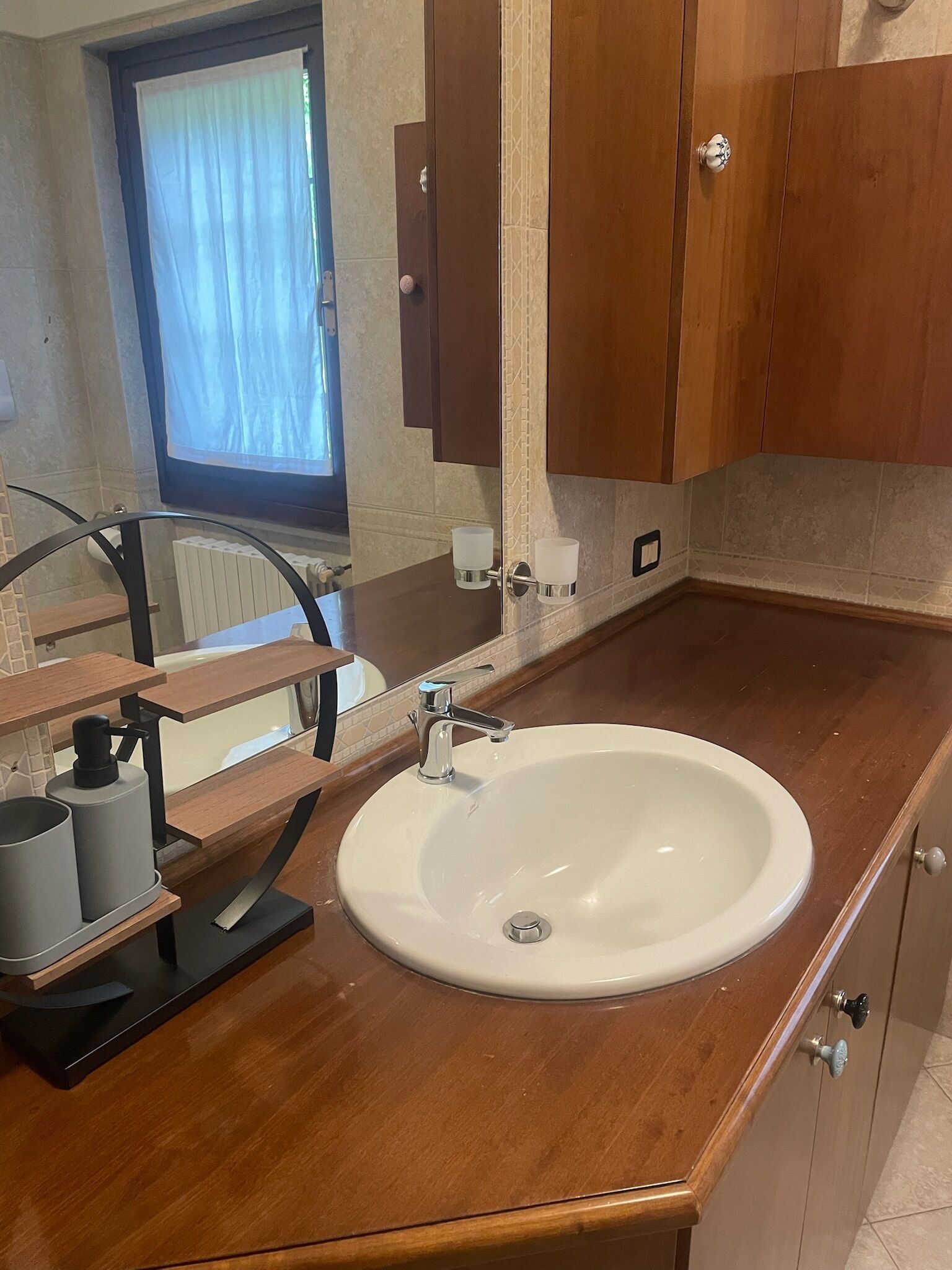 A bathroom with a wooden vanity, a white sink, and a mirror.