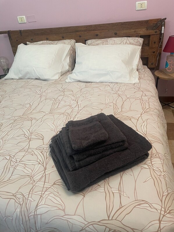A neatly made bed with a floral-patterned bedspread, two white pillows, and a stack of folded dark towels. - Villa Vinea Prisca  (Cenate Sotto)