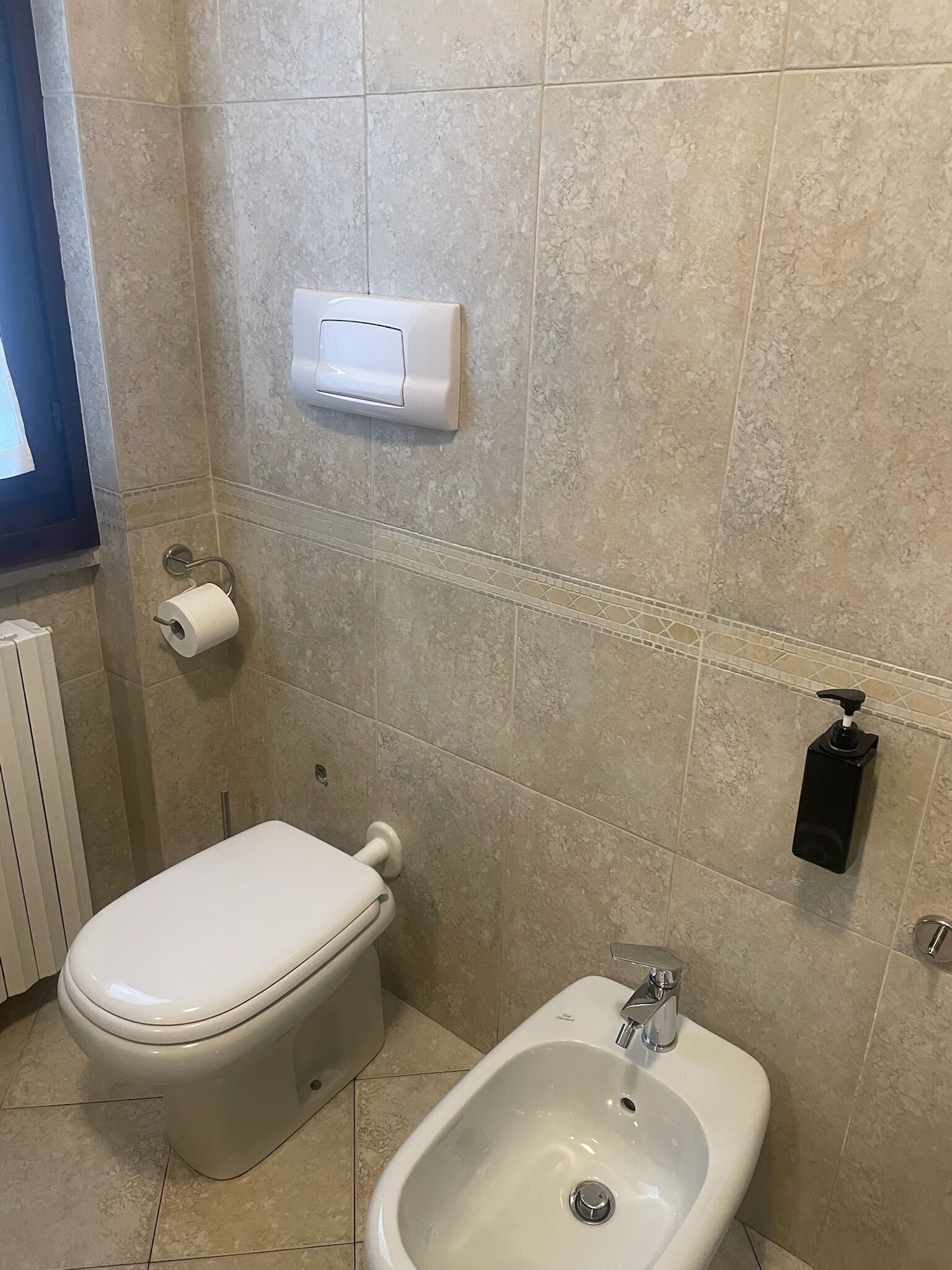 Un baño con inodoro, bidé y un secador de manos en la pared.