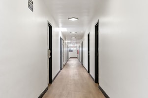 Un largo pasillo estrecho con puertas a ambos lados, piso de color claro e iluminación empotrada en el techo.