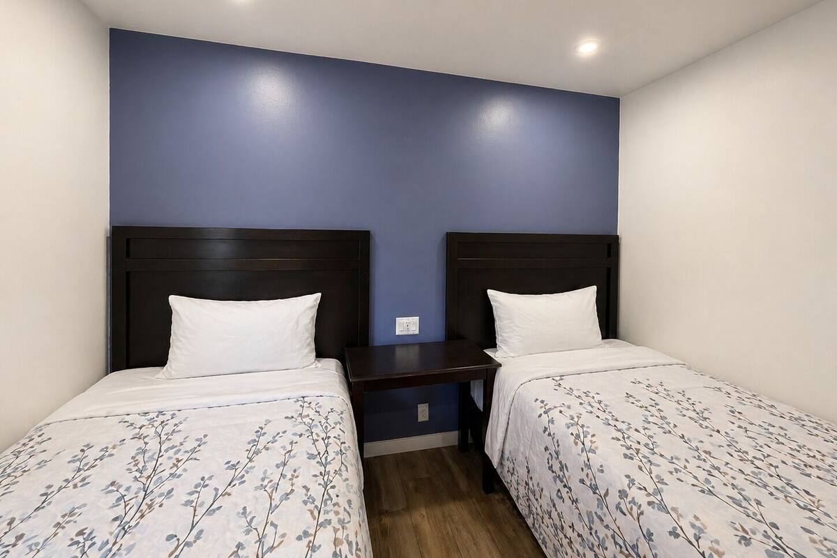 A room with two beds, each with a dark headboard and white bedding.