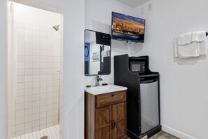 A bathroom with a shower, sink, mirror, and a television mounted on the wall. - Encore Inn Inglewood  (Inglewood)