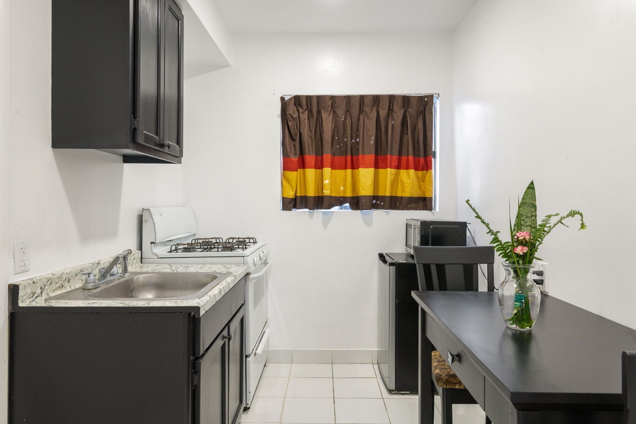 Een compacte keuken met een gasfornuis, spoelbak en een klein eethoekje met een tafel en stoelen.