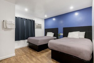 Habitación de hotel con dos camas, cortina de ducha, aire acondicionado montado en la pared y una toalla blanca en la pared.