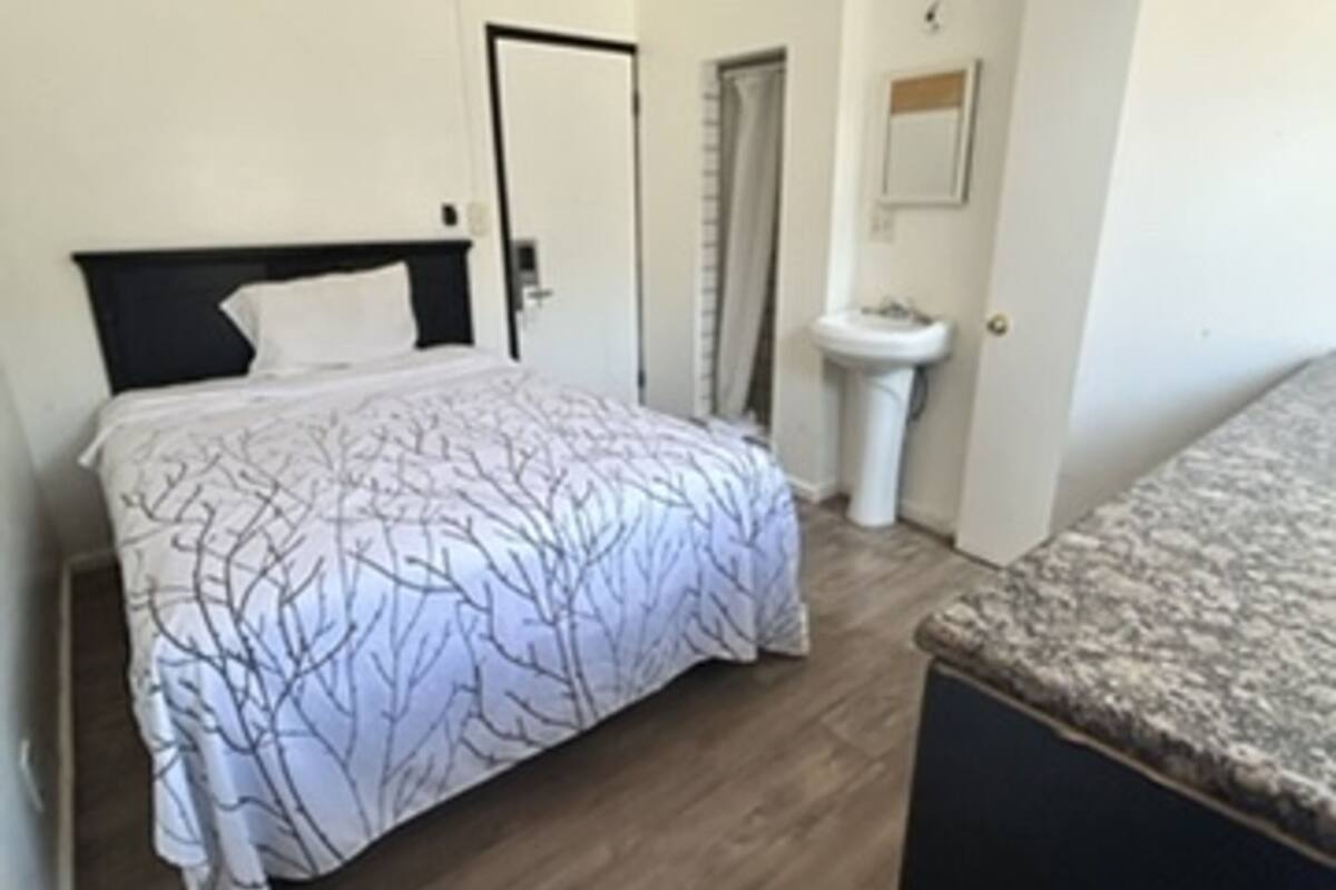 A bedroom with a bed, a door, a bathroom with a sink, and a mirror.