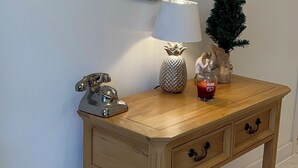 A wooden console table with a mirror, a lamp, a small Christmas tree, and a decorative telephone.