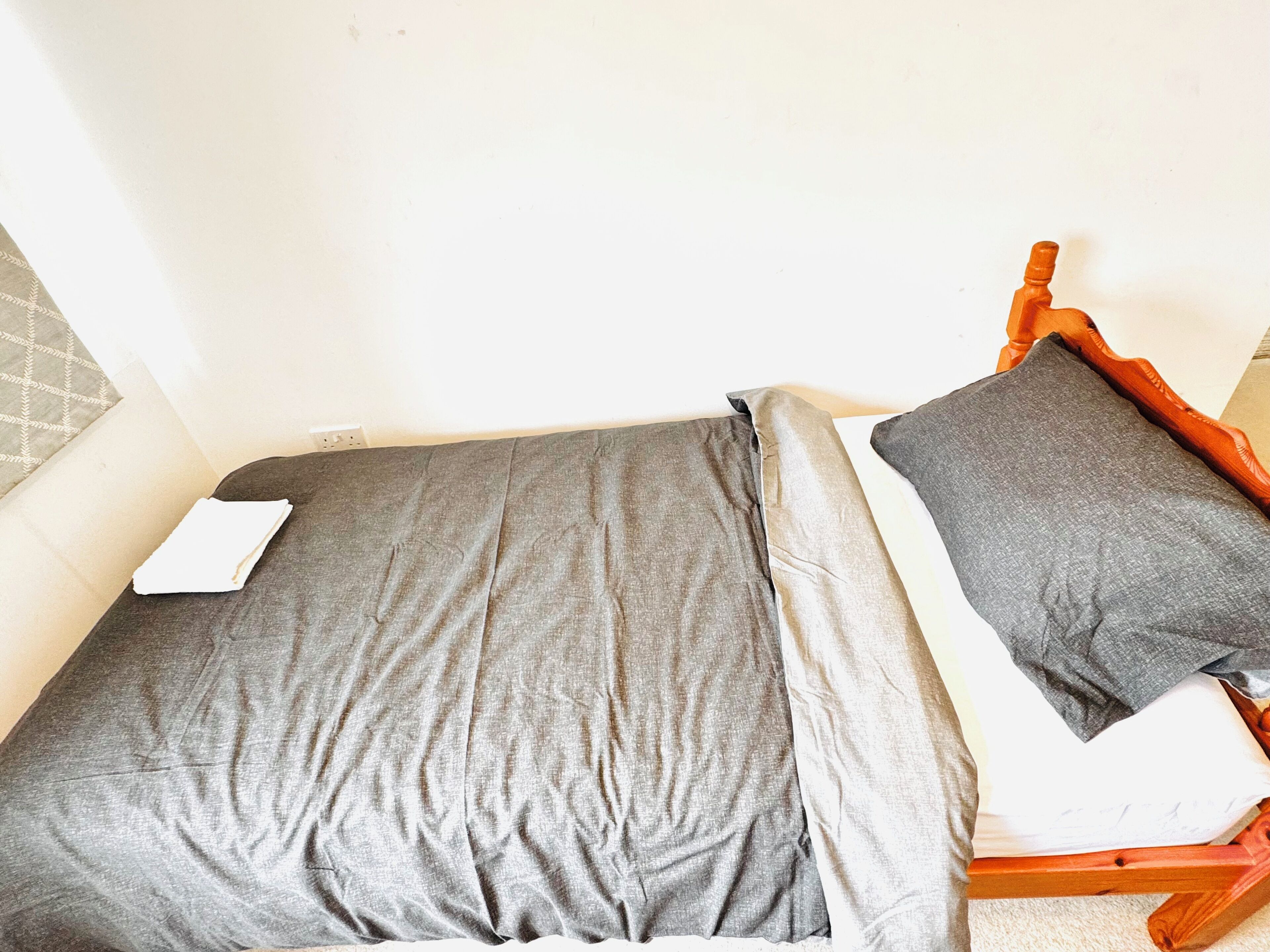 Une petite chambre avec un lit simple, une tête de lit en bois et une couvre-lit grise.