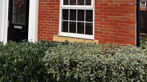 A red brick house with a black front door, two windows with white frames, and a small security light.