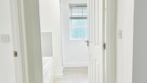 A hallway with white walls, a tiled floor, and a door leading to a room with a window.