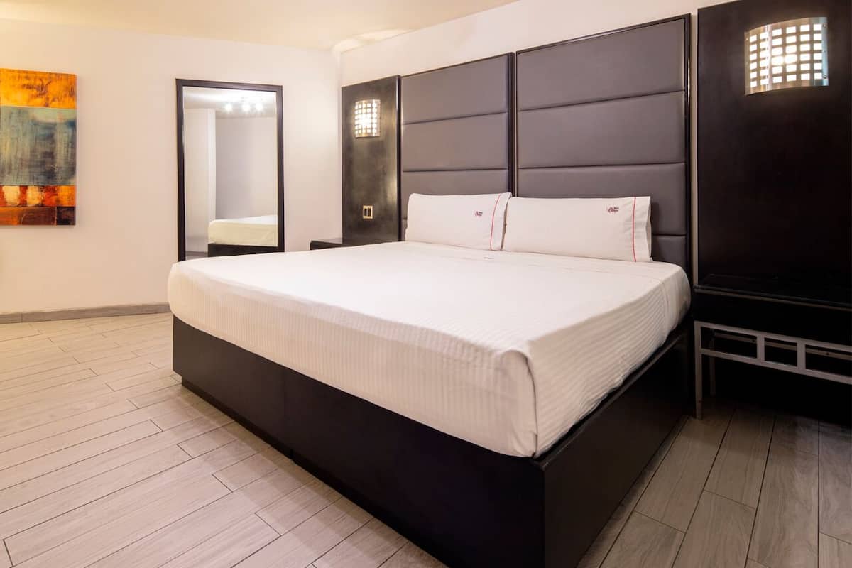 A modern bedroom with a large bed, a dark headboard, and a light-colored floor.