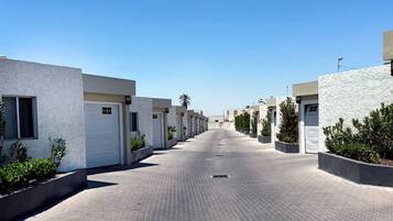 A row of modern, white buildings with uniform doorways and windows, arranged along a paved pathway.