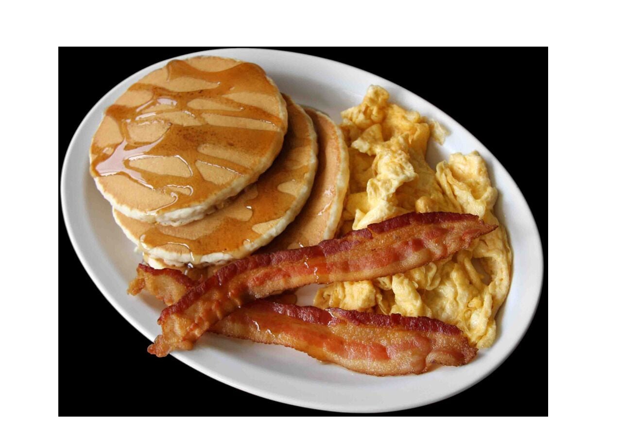 A plate with pancakes, scrambled eggs, and bacon.