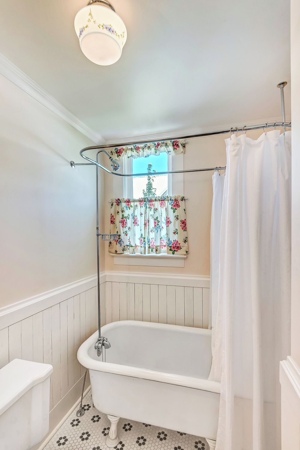 A bathroom with a clawfoot bathtub, a window with floral curtains, and a shower curtain.
