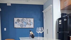 A kitchen with a blue wall, a wooden table with shelves, a chair, a wine bottle, and two wine glasses. - Charming Modern 1-bedroom apartment with WiFi, AC in Beautiful Nassau (Nassau)