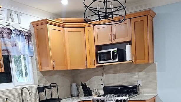 A modern kitchen with wooden cabinets, a central island with bar stools, a microwave, a stove, and a pendant light. - Charming Modern 1-bedroom apartment with WiFi, AC in Beautiful Nassau (Nassau)