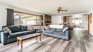 Een ruime woonkamer met twee grijze banken, een houten salontafel en een plafondventilator.