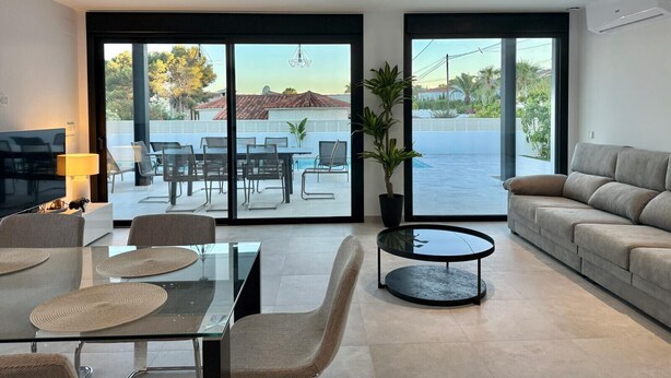 A modern living room with a glass dining table, comfortable seating, a sofa, and large sliding glass doors leading to a pool area. - Vallesa II  - Modern villa with private pool (Calpe)
