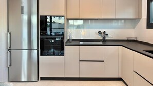 A modern kitchen with a stainless steel refrigerator, a built-in oven, and a black countertop. - Vallesa II  - Modern villa with private pool (Calpe)