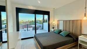 A modern bedroom with a large bed, a nightstand, a desk, and a view of the outside. - Vallesa II  - Modern villa with private pool (Calpe)
