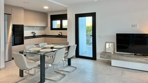 A modern kitchen with a glass dining table, built-in appliances, and a large TV. - Vallesa II  - Modern villa with private pool (Calpe)