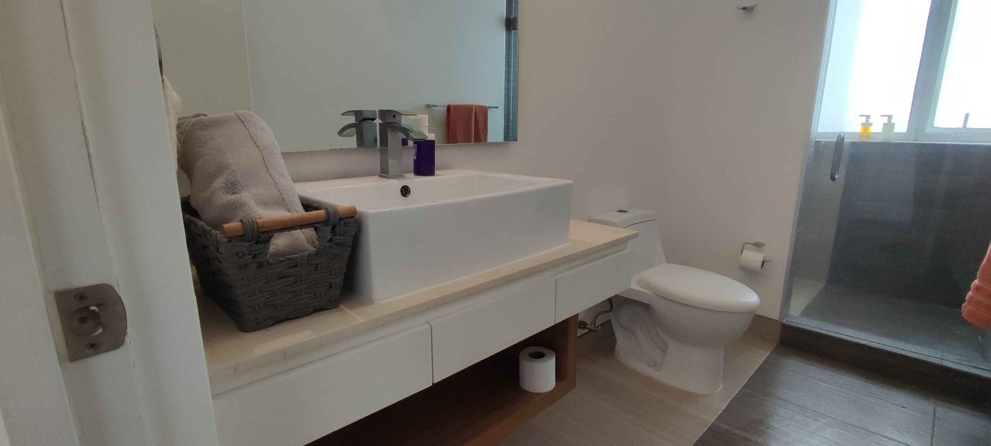 Un baño con lavamanos blanco, espejo, toalla y retrete.