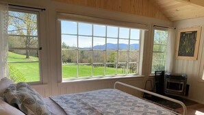 Una camera da letto con un'ampia finestra, un letto, un caminetto e vista su un paesaggio verde.