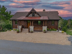 Une cabane rustique en rondins de bois, dotée d’une entrée en pierre, d’un porche en bois et d’une allée gravillonnée.