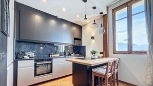 A modern kitchen with dark cabinets, a marble backsplash, and a wooden dining area with a view of the mountains.