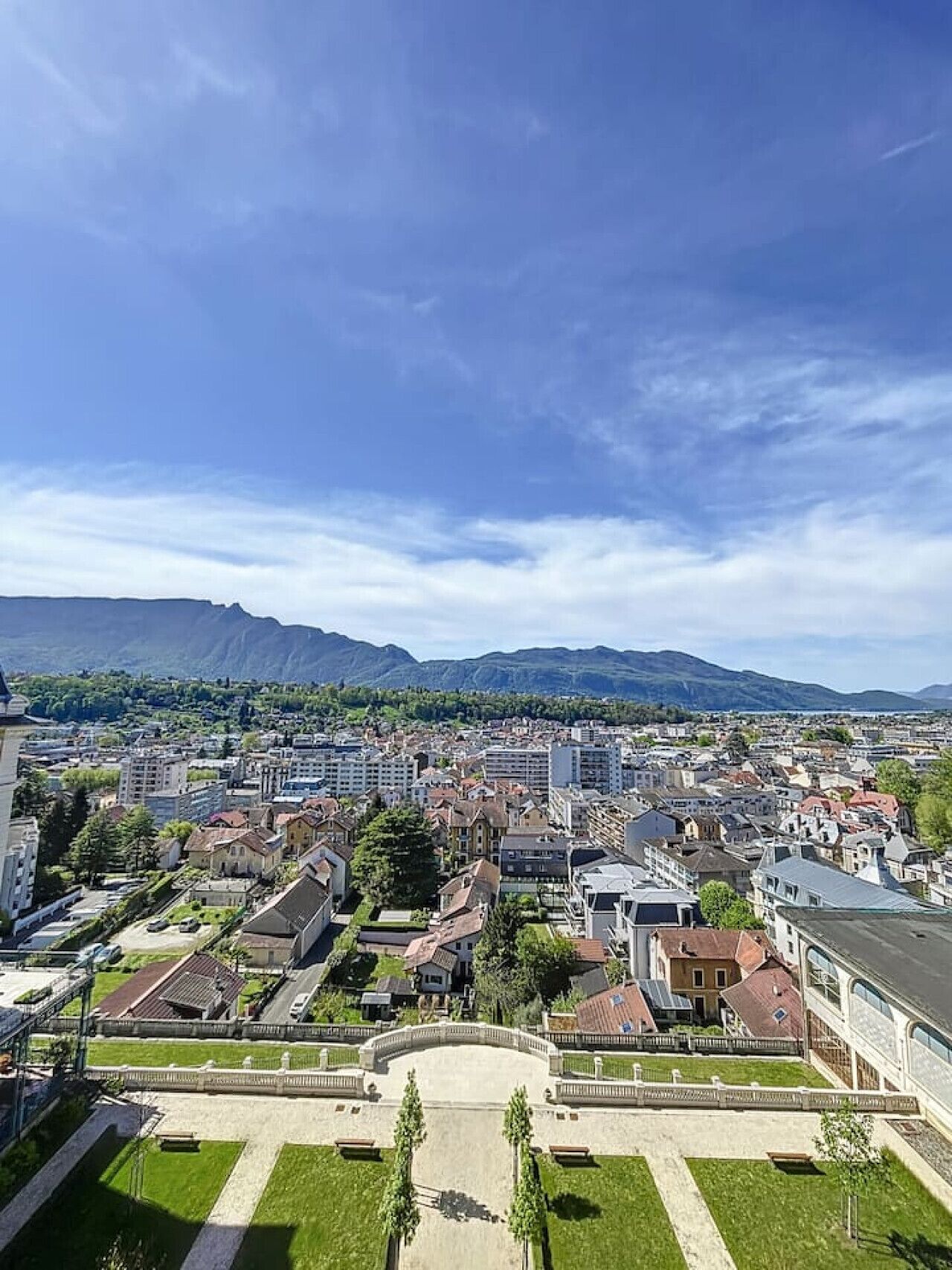 Un barrio residencial con casas y edificios de apartamentos, un parque central y montañas al fondo.