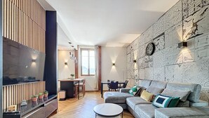 A modern living room with a sofa, a coffee table, and a TV. There is a dining area with a table and chairs.
