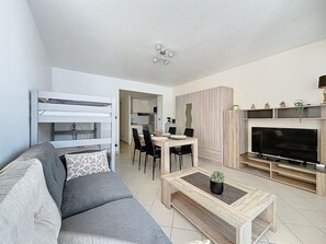 Een moderne woonkamer met een grijze bank, een houten salontafel, een televisie en een eethoek met stoelen en een tafel.