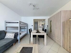 Un espace de vie compact comprenant des lits superposés, une table à manger et un coin cuisine.