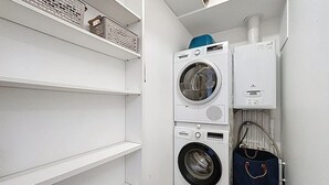 A laundry room with two stacked washing machines and a dryer, a shelf with baskets, and a hanging bag. - Brison-Saint-Innocent - L'Instant paisible (Brison-Saint-Innocent)