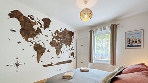 A bedroom with a world map wall, a bed with pillows, a window with curtains, and a hanging light fixture. - Brison-Saint-Innocent - L'Instant paisible (Brison-Saint-Innocent)