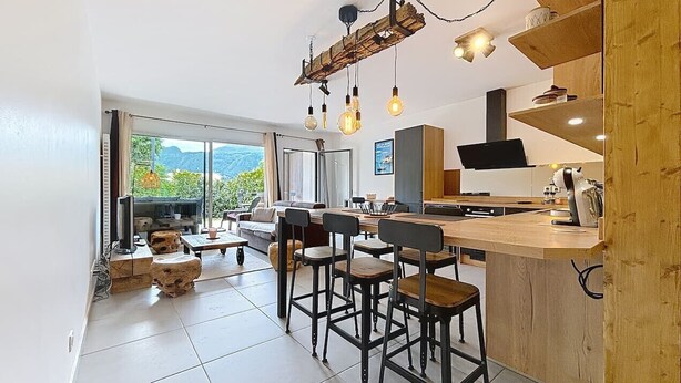 A modern kitchen with a wooden bar area, a dining set, and a large window offering a view of the outdoors. - Brison-Saint-Innocent - L'Instant paisible (Brison-Saint-Innocent)