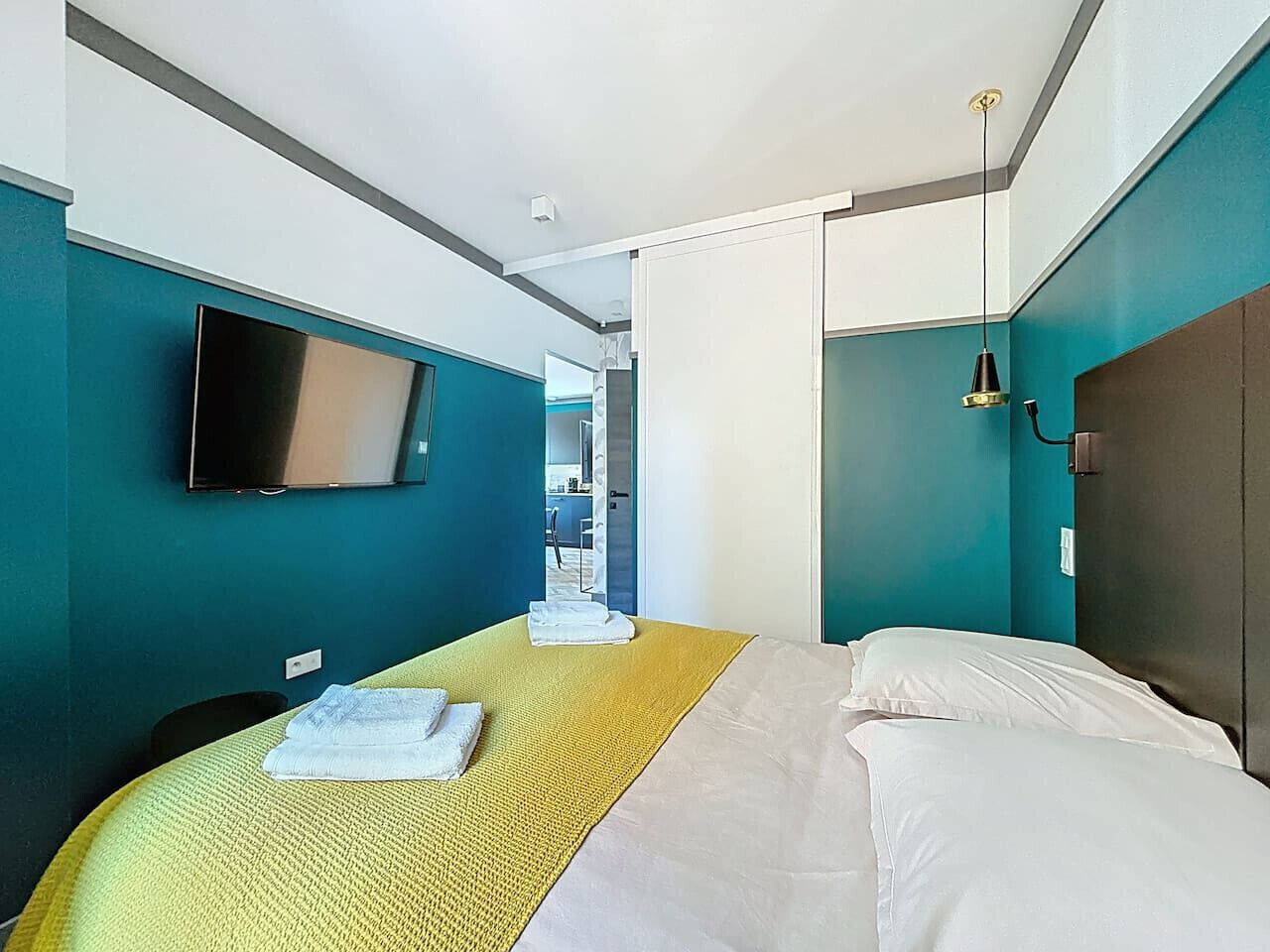Une chambre d’hôtel moderne, équipée d’un lit, d’un téléviseur fixé au mur et offrant une vue sur le couloir.