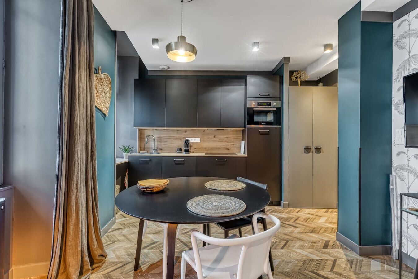 Una cocina moderna con armarios oscuros, una mesa redonda de comedor con dos sillas y una lámpara colgante.
