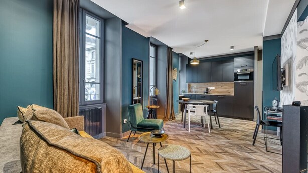 En moderne stue med sofa, spisebord og stole. Der er et køkken med køleskab og mikrobølgeovn.