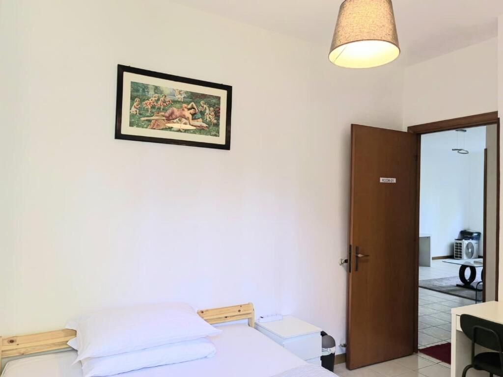 Una habitación de hotel con una cama, una mesita de noche, una lámpara y una puerta que da al baño.