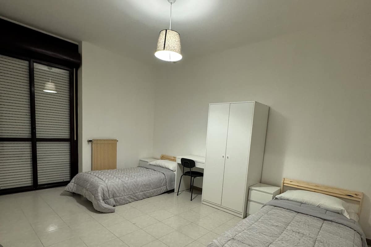 A bedroom with two beds, a desk, a wardrobe, and a radiator.